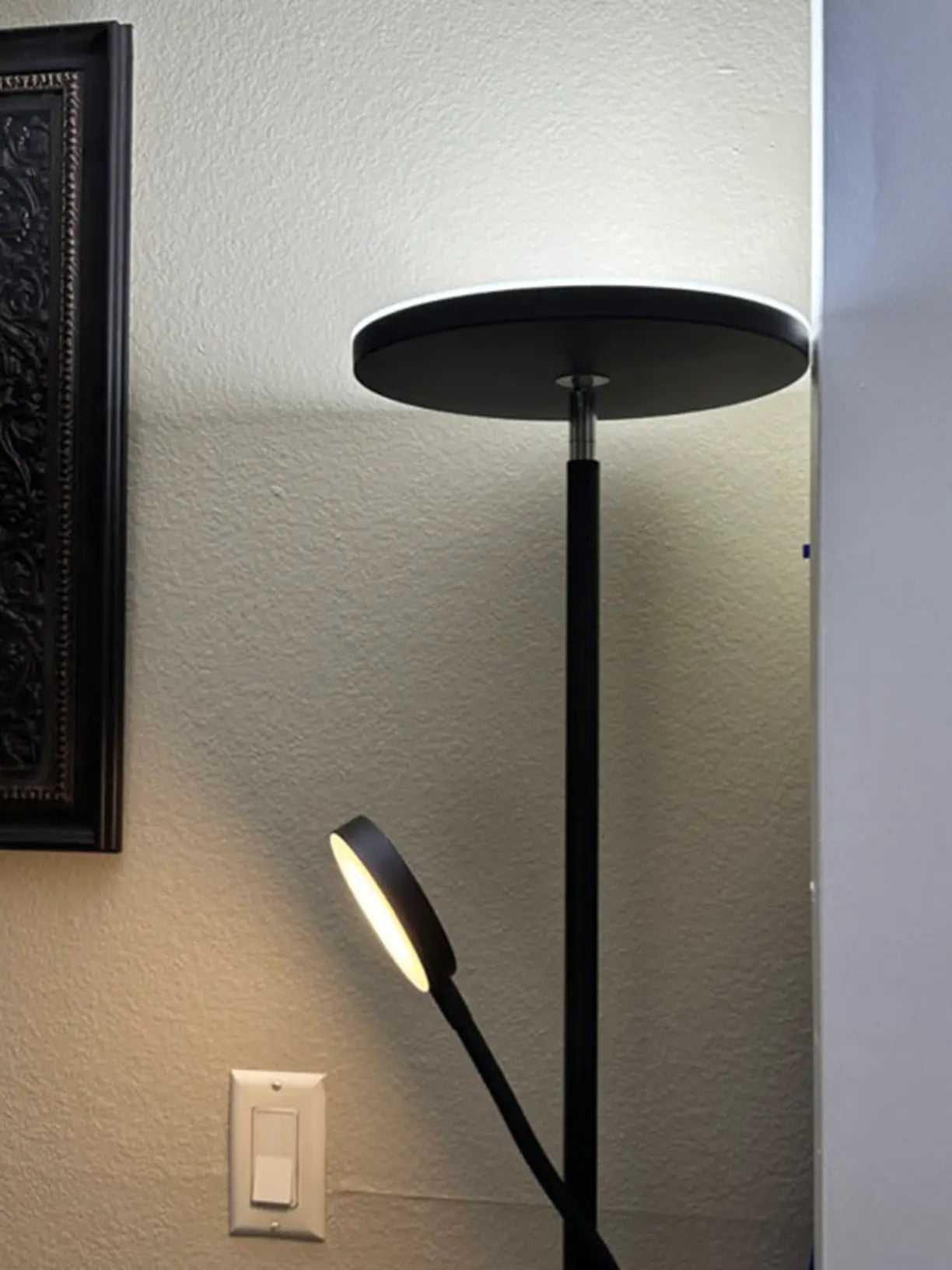 A classic torchiere floor lamp with an elegant black finish, providing widespread ambient light from its main head and focused light from its adjustable reading arm, enhancing a traditional living space.