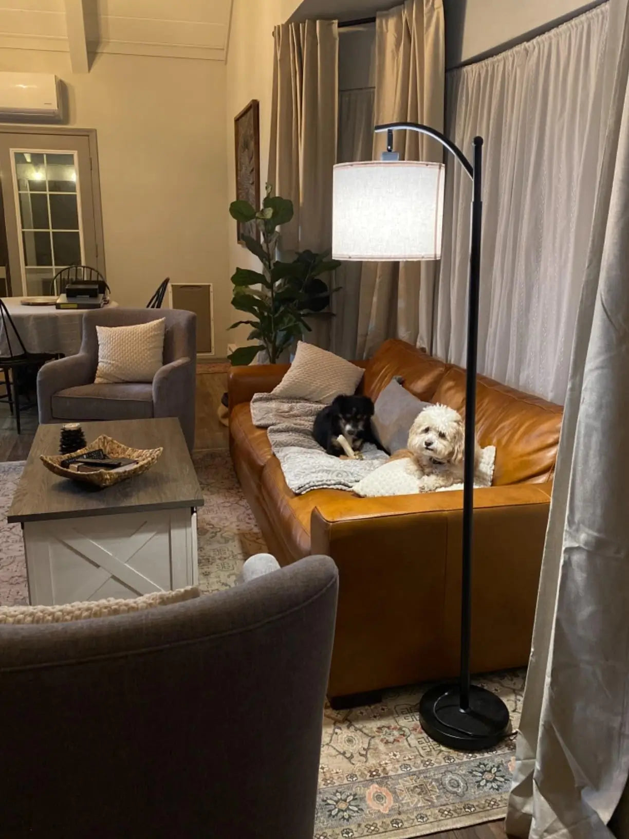 A contemporary bronze-finished arc lamp with a wide, white fabric shade arching over a gray sofa, creating a stylish and inviting lighting solution for a modern living room.