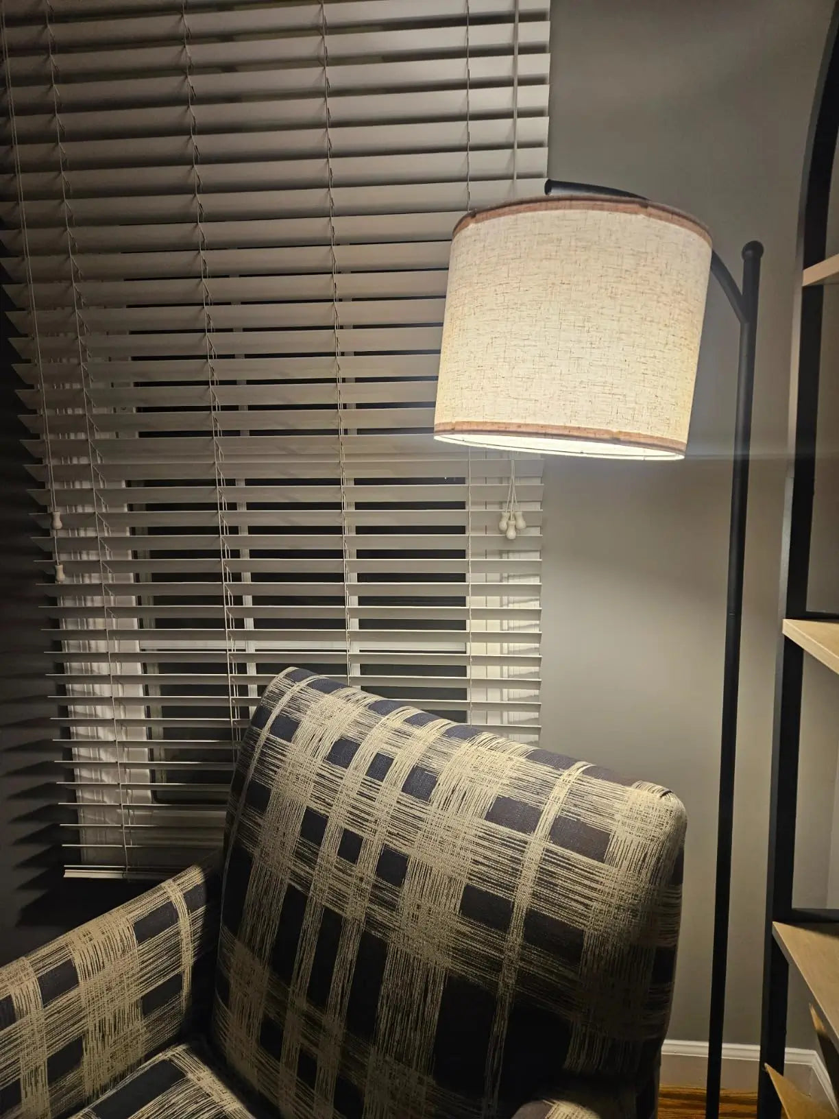 A minimalist black arc floor lamp with a simple black metal shade, positioned beside a bed with white bedding, providing focused lighting for reading or accenting the bedroom decor.