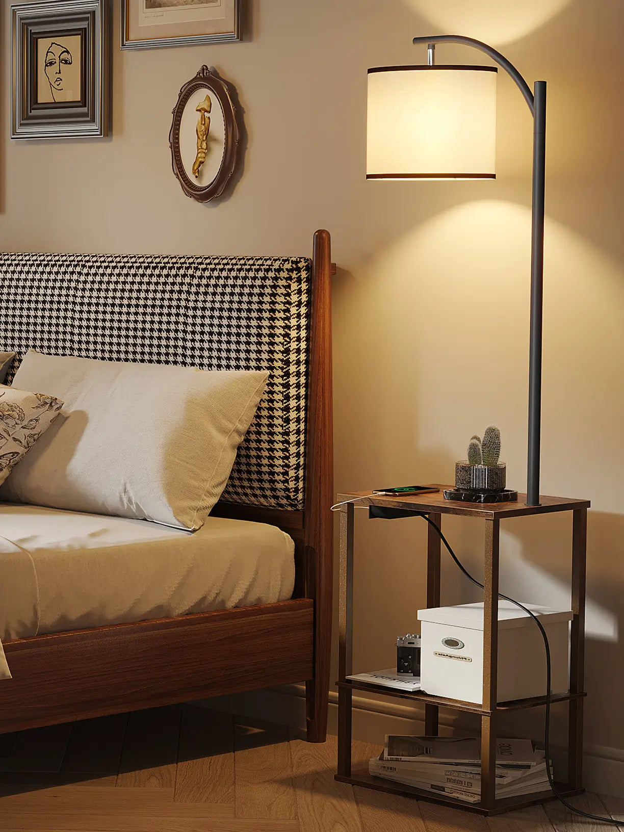 A modern bedroom floor lamp with a curved arm and a neutral-toned shade, featuring a built-in side table with shelves and charging capabilities, placed beside a stylish bed.