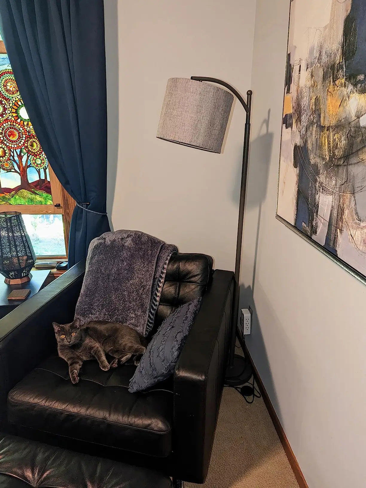 A sleek black arched floor lamp with a simple shade, extending over a modern dining table with four chairs and decorative elements, ideal for focused overhead illumination.