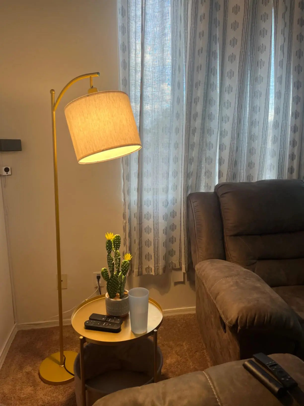 A tall arc floor lamp with a luxurious gold-finished base and a clean white drum shade, gracefully arching over a cozy bed in a bedroom, offering elegant lighting.